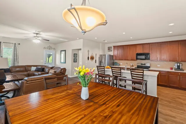 a kitchen with stainless steel appliances kitchen island granite countertop a stove a refrigerator a sink a dining table and chairs with wooden floor
