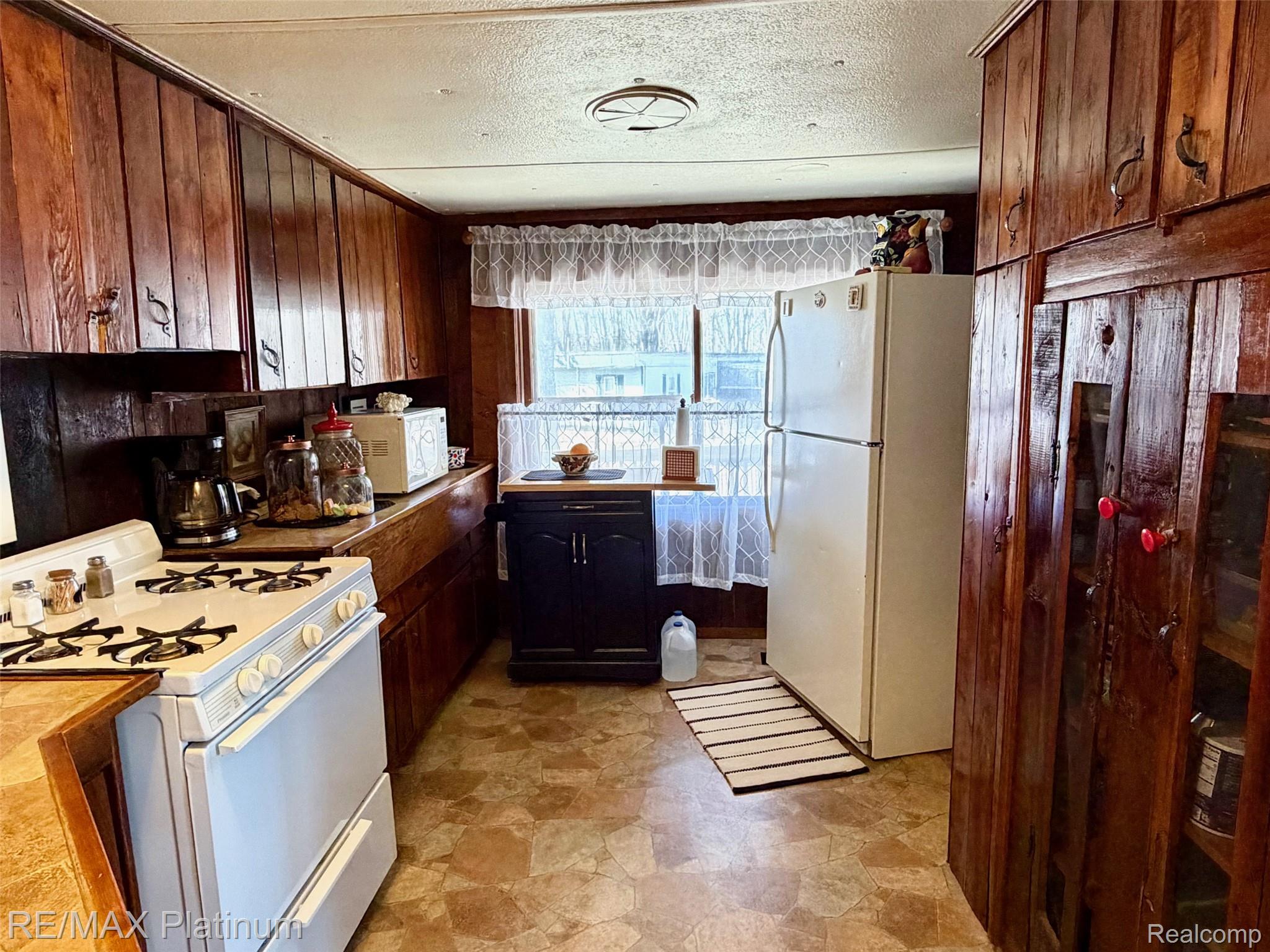 6787 Coon Hill Road Munith, MI 49259 - Photo 4 of 21 Kitchen with white appliances, a textured ceiling, wooden walls, stone finish flooring, and dark wood finish cabinets