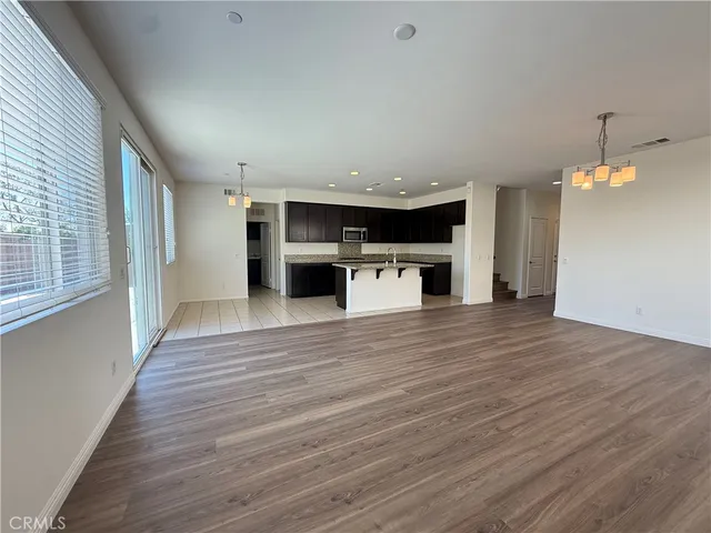an empty room with wooden floor kitchen view and a window
