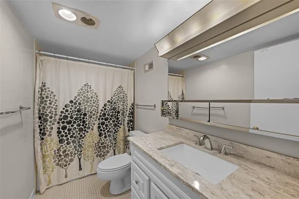 a bathroom with a granite countertop sink a toilet a mirror and shower curtain