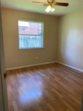 an empty room with wooden floor chandelier fan and windows