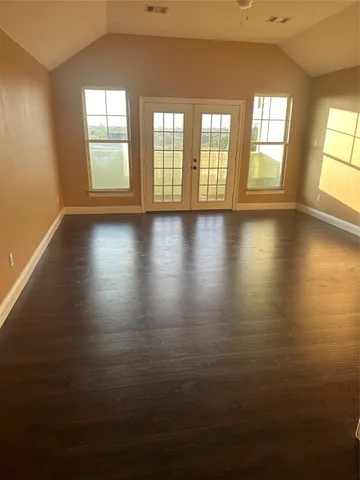 an empty room with wooden floor and windows with curtains