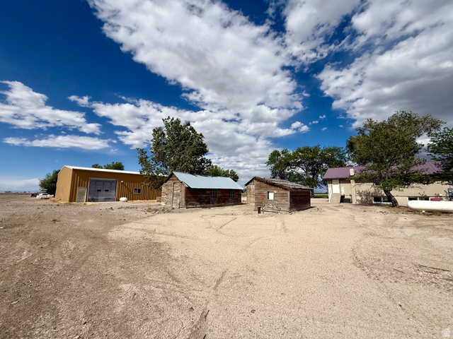 2865 North 3250 W Road Sutherland, UT 84624 - Photo 24 of 28 Expansive property featuring a large tan metal building with dual bay doors, two rustic wooden outbuildings with metal roofs, and a multi-level structure with a light-colored exterio