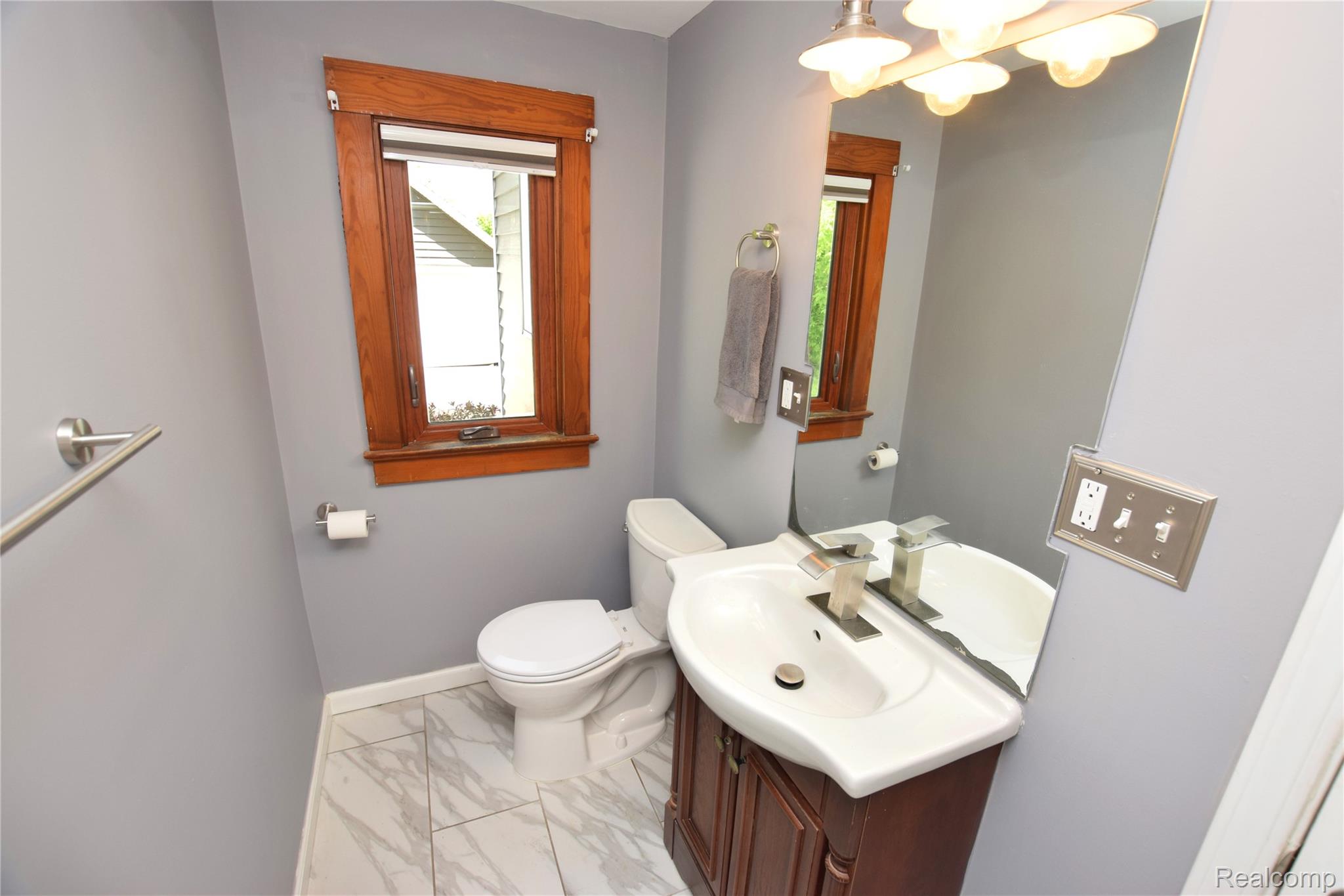 404 North Adelaide Street Fenton, MI 48430 - Photo 10 of 23 Bathroom featuring a wooden framed window, a toilet, a vanity with a white basin, a wall-mounted mirror, and tile flooring