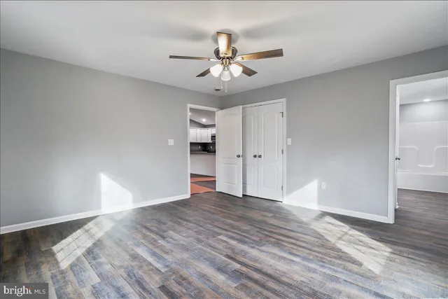 an empty room with wooden floor chandelier fan and windows