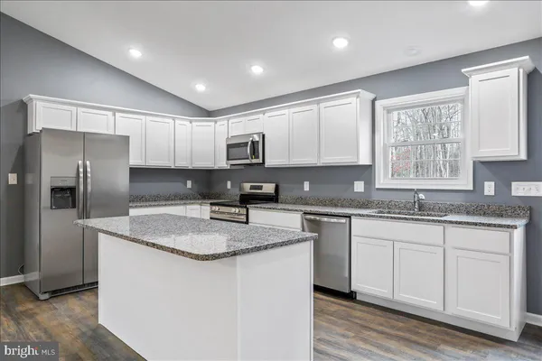 a kitchen with stainless steel appliances granite countertop a sink a stove top oven a refrigerator with white cabinets and wooden floor