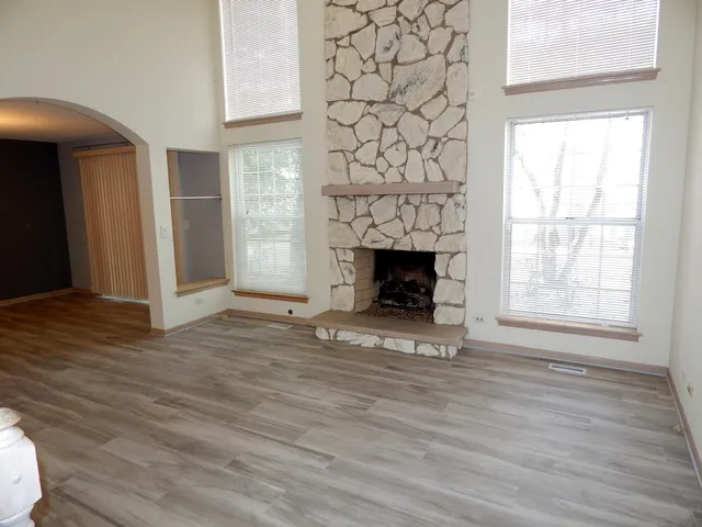 an empty room with wooden floor fireplace and windows