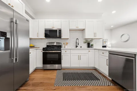 a kitchen with stainless steel appliances granite countertop a refrigerator a sink a stove and white cabinets with wooden floor