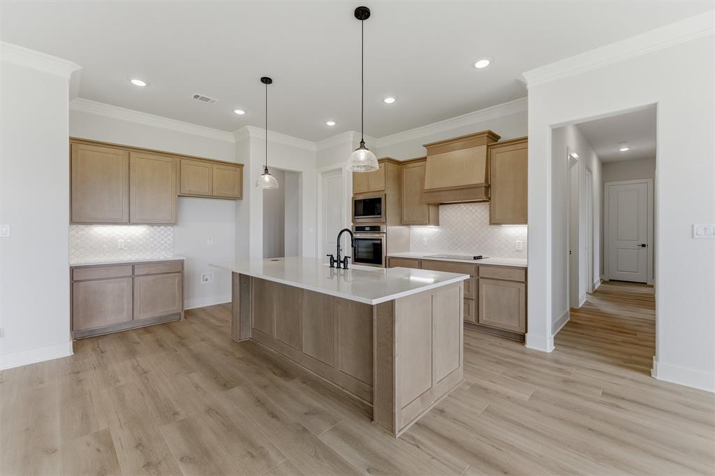 2204 Continent Court Krum, TX 76249 - Photo 17 of 28 Spacious kitchen featuring a large central island with a white solid surface countertop, light wood-finish cabinetry, built-in double ovens, and a white geometric tile backsplash