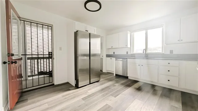 a kitchen with stainless steel appliances granite countertop a refrigerator a sink and white cabinets with wooden floor