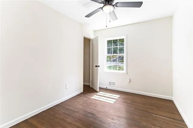 an empty room with wooden floor chandelier fan and windows