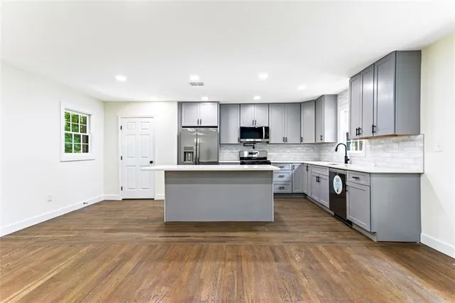a large kitchen with stainless steel appliances kitchen island granite countertop a stove a sink a refrigerator and white cabinets with wooden floor
