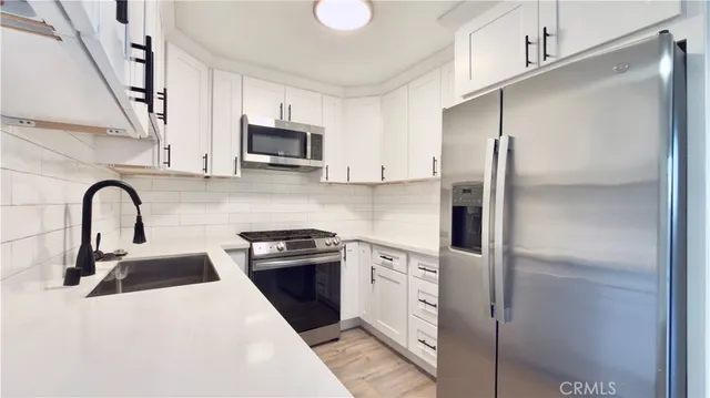 a kitchen with stainless steel appliances granite countertop a refrigerator a sink a stove and white cabinets with wooden floor