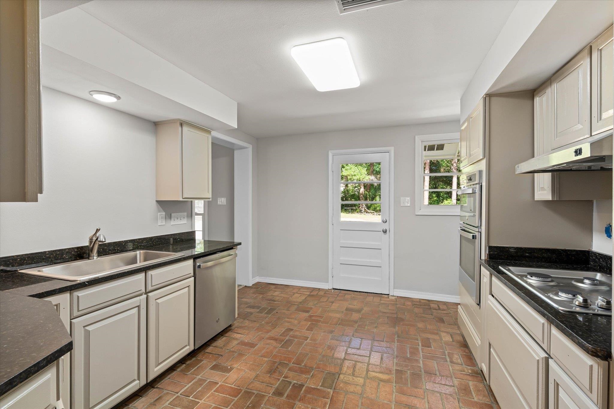 4700 Bit And Spur Road Mobile, AL 36608 - Photo 7 of 21 Kitchen with under cabinet range hood, a sink, brick floor, baseboards, and appliances with stainless steel finishes