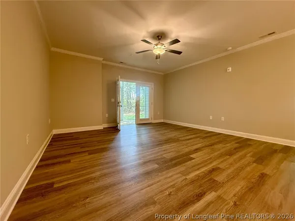 a view of an empty room with wooden floor and a fan