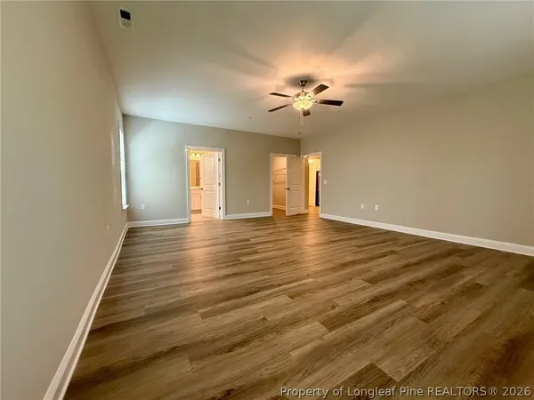a view of an empty room with chandelier fan and wooden floor