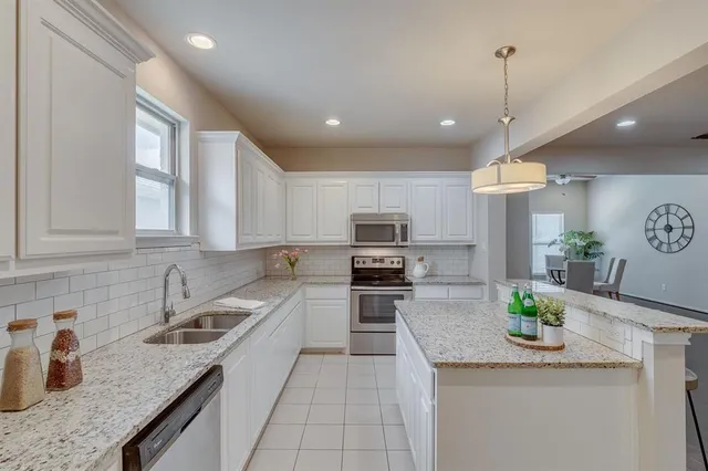 a kitchen with granite countertop stainless steel appliances a sink a counter top space cabinets and a potted plant