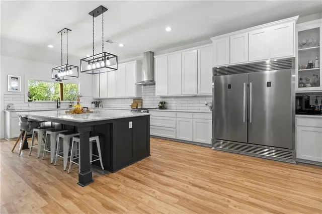 a kitchen with stainless steel appliances granite countertop a refrigerator a sink dishwasher a stove and white cabinets with wooden floor