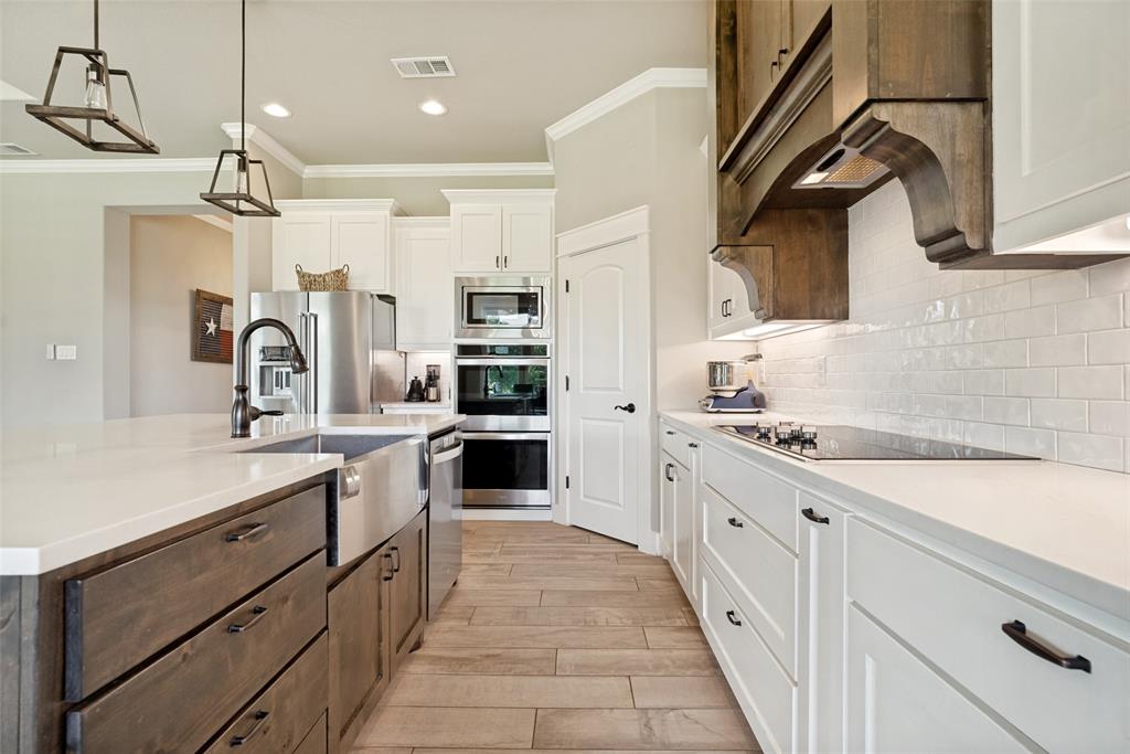 6913 Veal Station Road Weatherford, TX 76085 - Photo 10 of 31 Kitchen featuring dual-toned cabinetry, a large center island with a stainless steel farmhouse sink, white subway tile backsplash, and integrated stainless steel appliances including a built-in microwave and double ovens