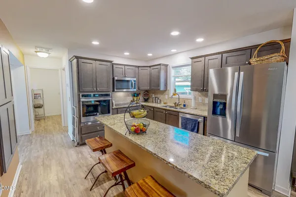 a kitchen with stainless steel appliances granite countertop a refrigerator oven a sink dishwasher and a stove with wooden floor