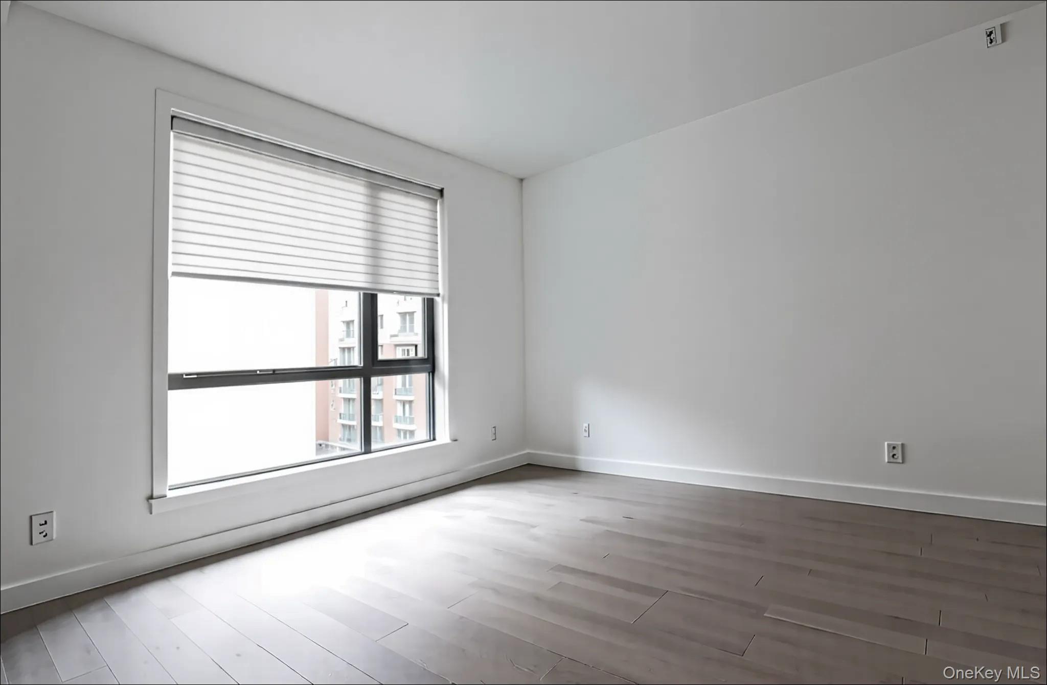 41-04 27th Street, Unit 9C Queens, NY 11101 - Photo 2 of 11 an empty room with wooden floor and windows