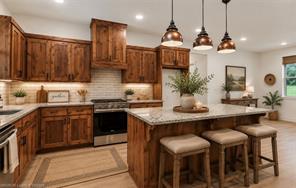 6138 New Hope Road Hackett, AR 72937 - Photo 6 of 56 Spacious kitchen featuring wood cabinetry, stainless steel range, white subway tile backsplash, and a large island with a stone countertop and pendant lighting