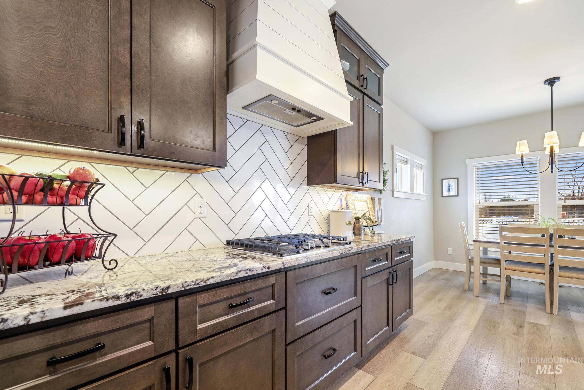 3103 Moonrise Road Twin Falls, ID 83301 - Photo 10 of 40 Kitchen with light stone counters, dark wood finish cabinetry, light wood-style floors, backsplash, and stainless steel gas stovetop