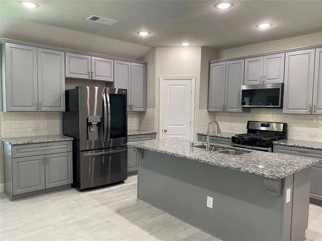 a kitchen with stainless steel appliances granite countertop a refrigerator a stove a sink and a microwave