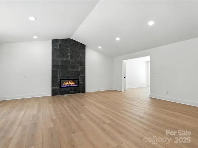 a view of an empty room with wooden floor and kitchen