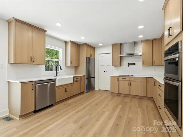 a large kitchen with a stove a sink dishwasher a refrigerator and white cabinets with wooden floor