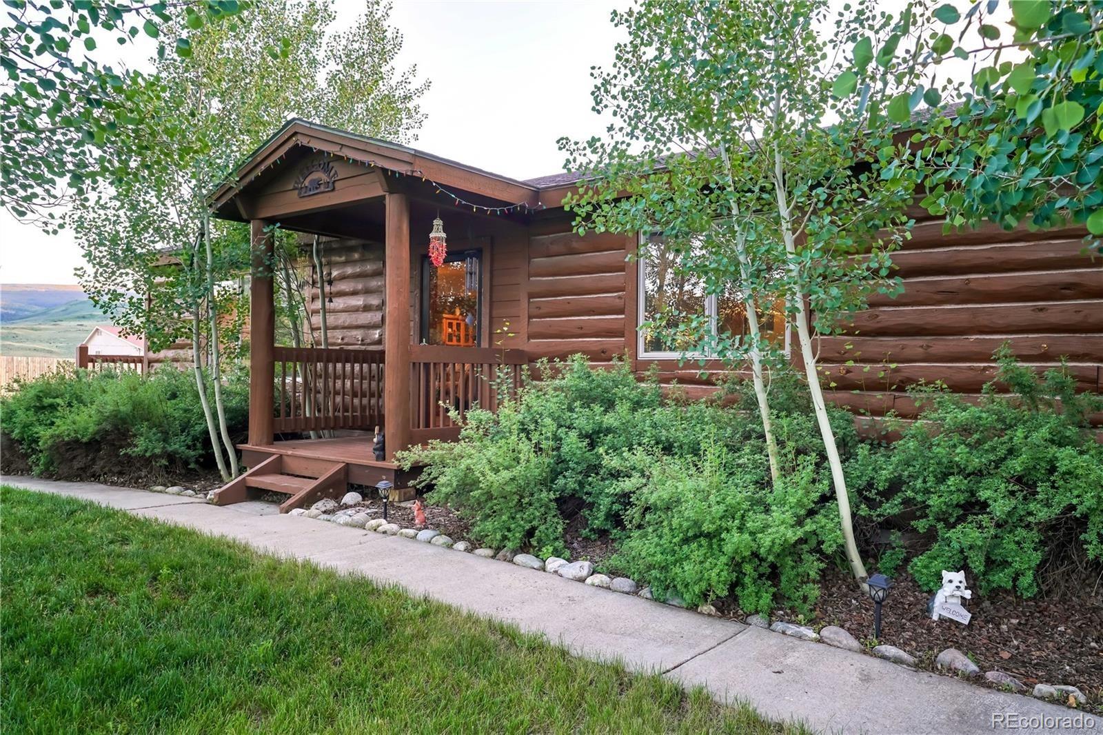 a view of a wooden house with a small yard plants and large trees