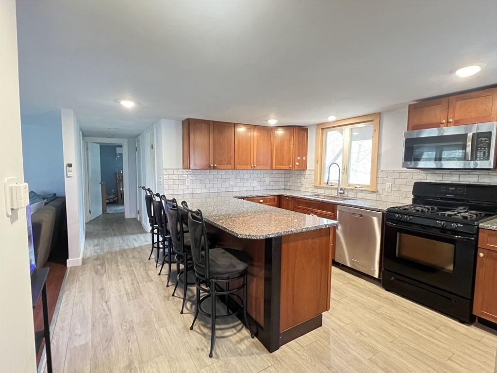 300 Main Road Colrain, MA 01340 - Photo 5 of 41 a kitchen with stainless steel appliances granite countertop a stove a refrigerator a sink a dining table and chairs with wooden floor