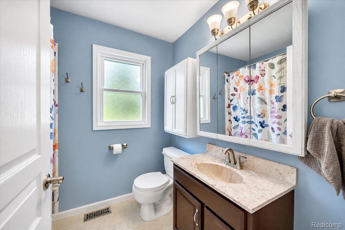 3852 North Lapeer Road Lapeer, MI 48446 - Photo 13 of 17 Bathroom featuring a single-sink vanity with a light-toned countertop, a three-door mirrored medicine cabinet, and overhead lighting