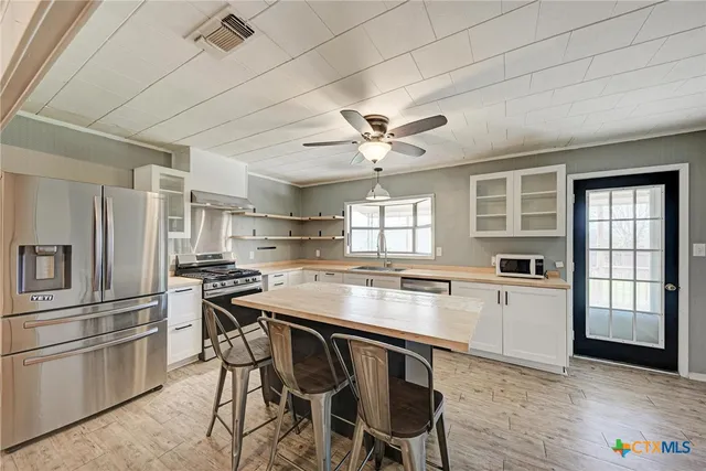 a kitchen with stainless steel appliances granite countertop a stove a refrigerator a sink a dining table and chairs with wooden floor