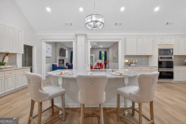 a kitchen with stainless steel appliances kitchen island granite countertop a refrigerator oven a sink dishwasher and white cabinets with wooden floor