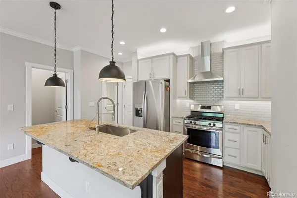 a kitchen with stainless steel appliances granite countertop a kitchen island a stove a refrigerator a stove and white cabinets with wooden floor
