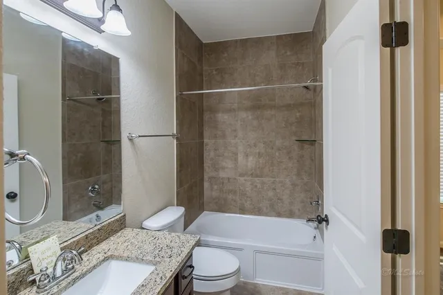 a bathroom with a granite countertop bathtub shower sink vanity and toilet