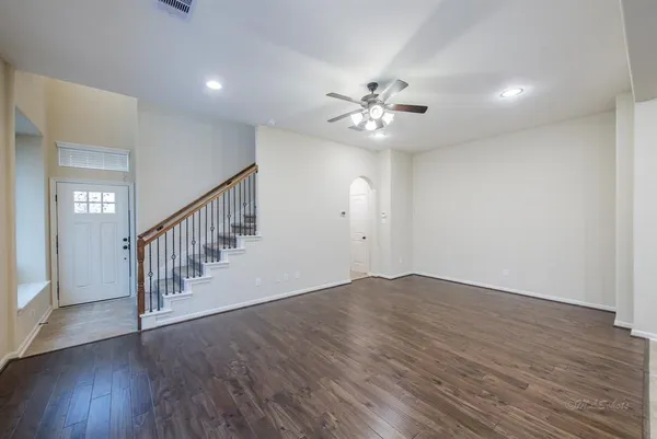 a view of an empty room with wooden floor and fan