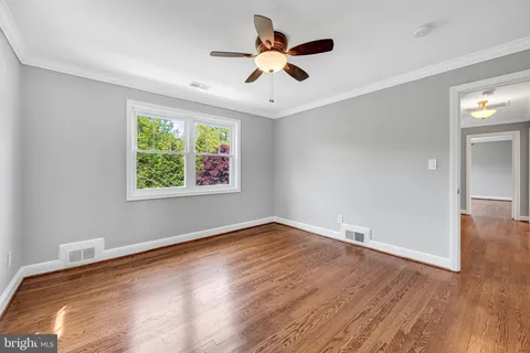 an empty room with wooden floor chandelier fan and windows