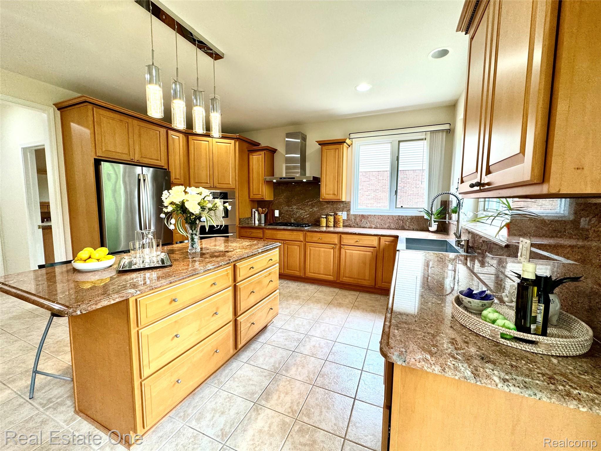 1215 Letica Drive Rochester, MI 48307 - Photo 6 of 43 Kitchen with light stone countertops, a center island, stainless steel appliances, hanging light fixtures, and backsplash