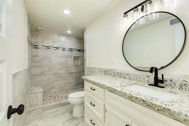 a bathroom with a granite countertop sink mirror vanity and toilet