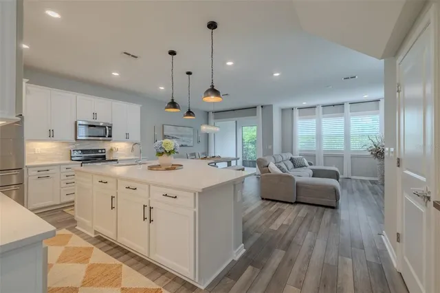 a large white kitchen with stainless steel appliances granite countertop a stove a sink a refrigerator and white cabinets with wooden floor