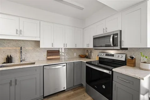 a kitchen with stainless steel appliances a white stove top oven a refrigerator white cabinets and wooden floor