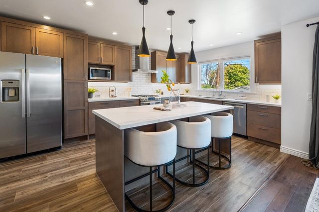 a kitchen with stainless steel appliances kitchen island granite countertop a table chairs sink and wooden floor