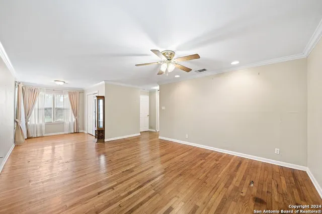 a view of an empty room with wooden floor and a ceiling fan