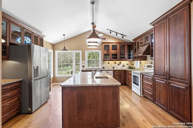 a large kitchen with stainless steel appliances granite countertop a refrigerator a sink dishwasher a stove and a dining table with wooden floor