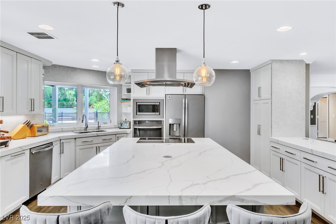 108 Quail Run Road Henderson, NV 89014 - Photo 27 of 50 Kitchen featuring island exhaust hood, light stone countertops, appliances with stainless steel finishes, hanging light fixtures, and white cabinets