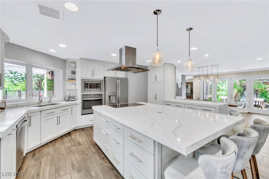 108 Quail Run Road Henderson, NV 89014 - Photo 4 of 50 Kitchen with island exhaust hood, light stone countertops, appliances with stainless steel finishes, hanging light fixtures, and a peninsula