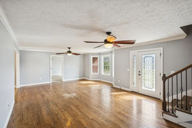 a view of an empty room with wooden floor and a ceiling fan