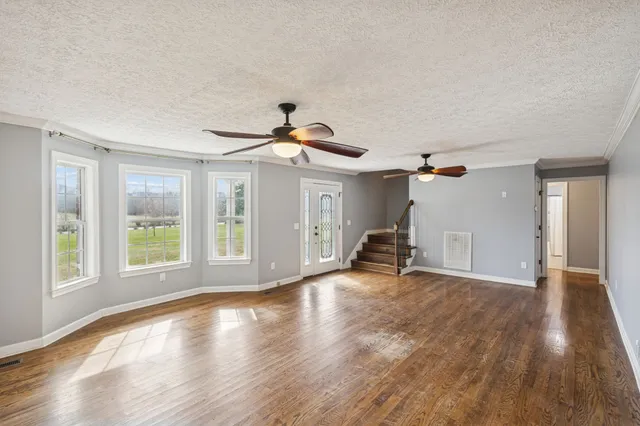 a view of empty room with wooden floor and fan